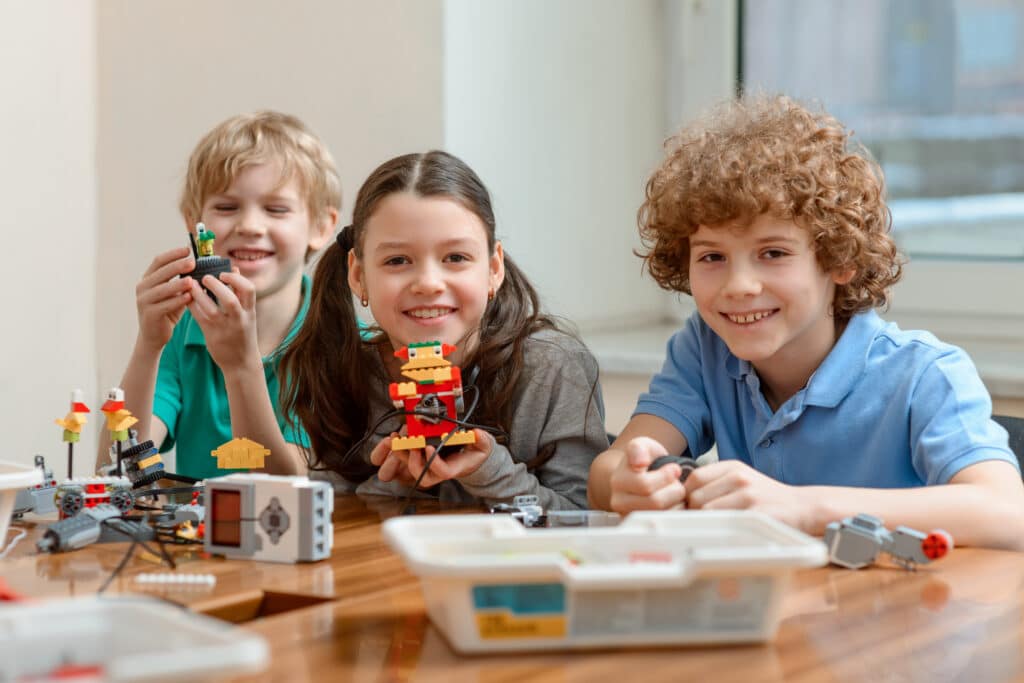 Cheerful Kids Showing Their Creations Made Of Plastic Blocks